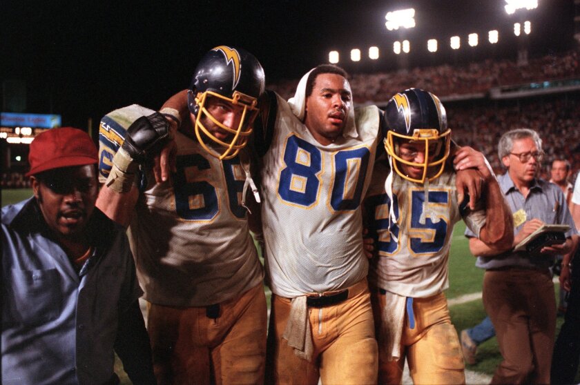 In what’s become a classic sports photo, a depleted Kellen Winslow (80) is helped off the field by teammates in the Chargers’ memorable playoff defeat of the Miami Dolphins in the Orange Bowl on Jan. 2, 1982. Photo by BOB IVINS