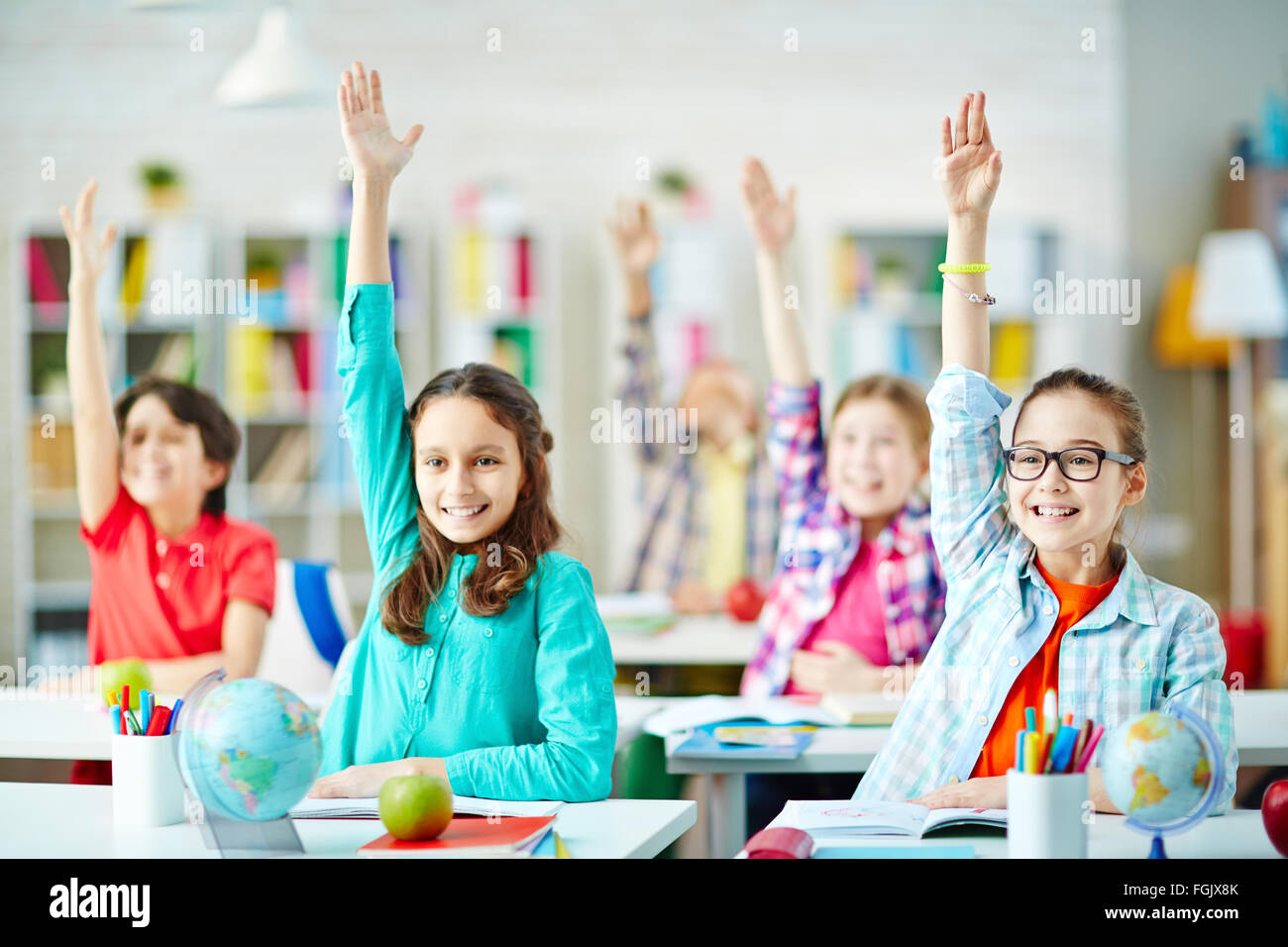 happy-pupils-sitting-by-desks-and-raising-hands-at-lesson-FGJX8K.jpg